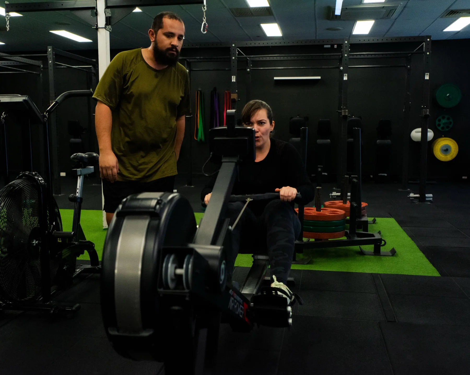Client rowing hard while a coach watches pace and form