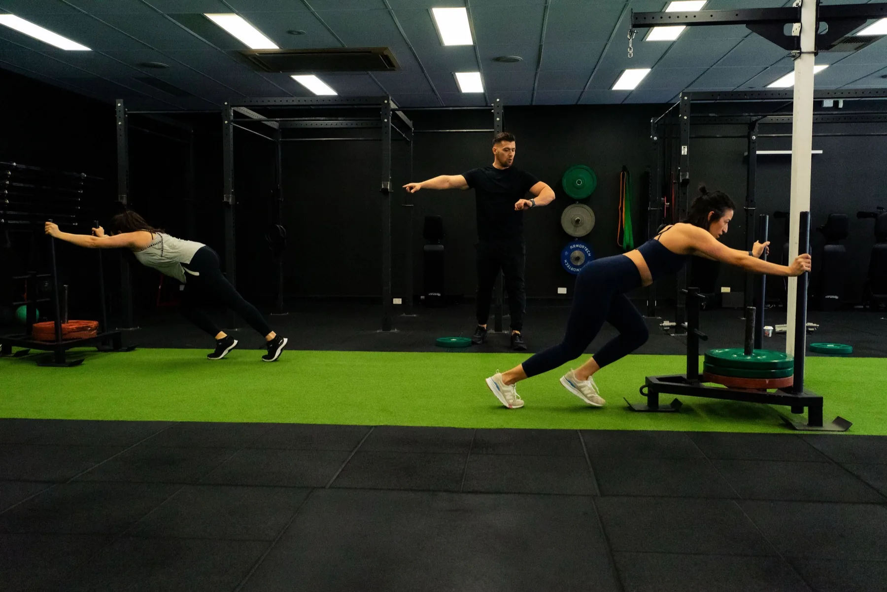 Clients pushing weighted sleds across the turf lane