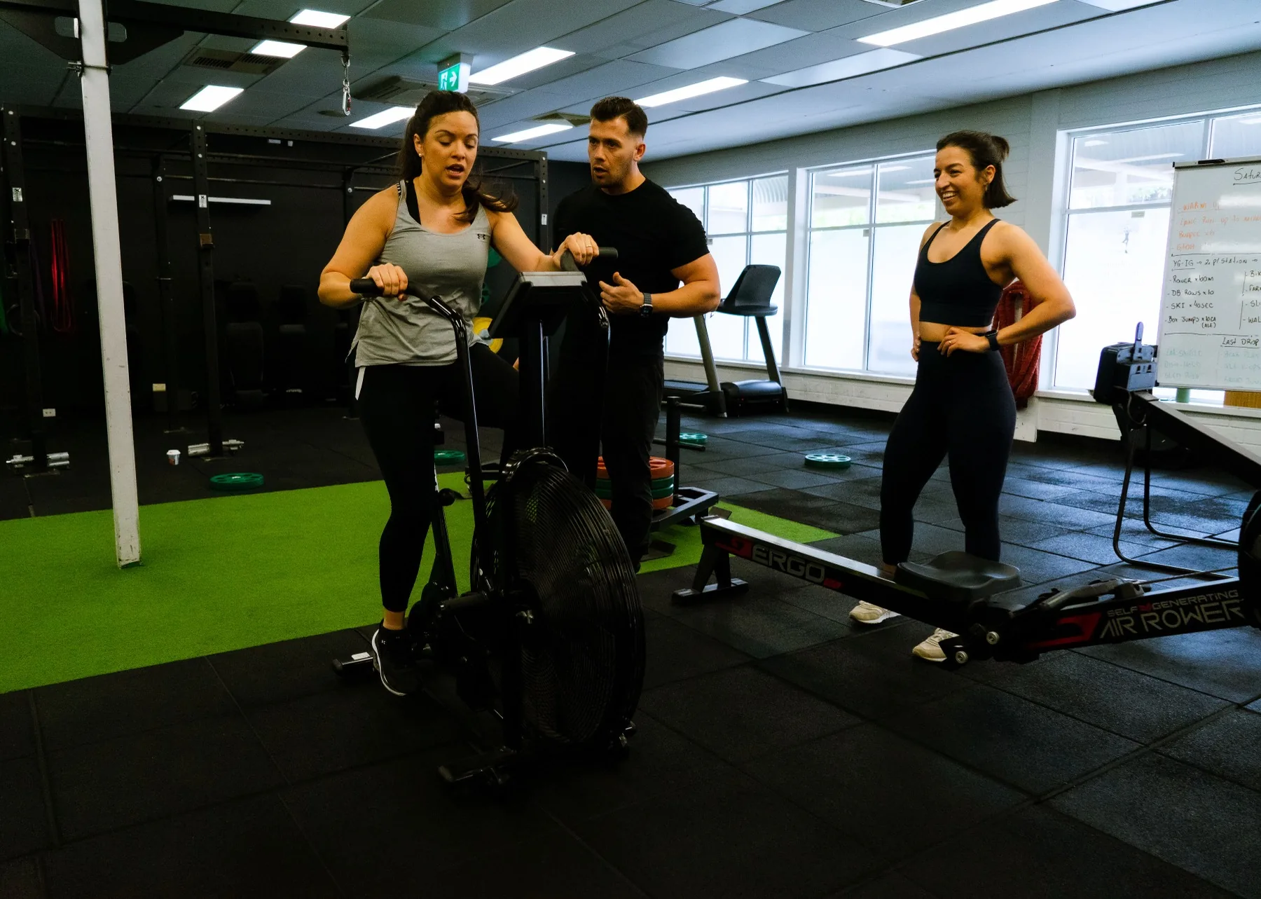 Client biking hard while Hudson coaches and another client watches